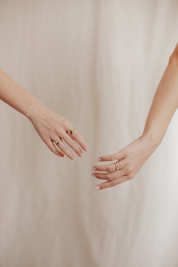 Artistic close-up of two elegant female hands wearing rings against a cream-colored backdrop.